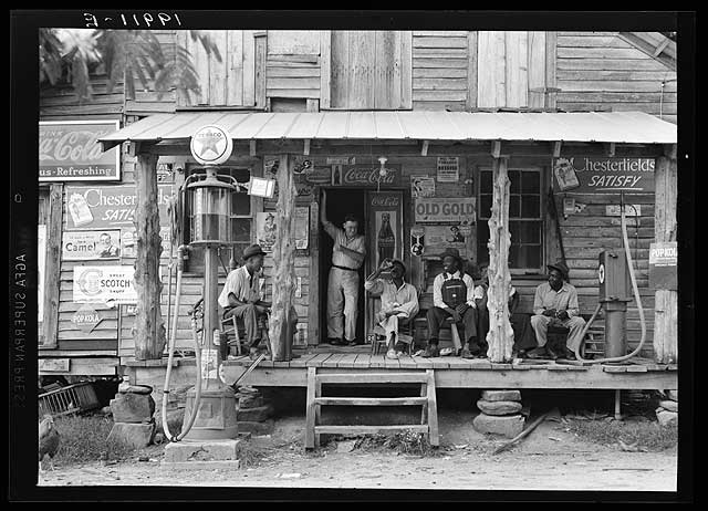Country store on dirt road. Sunday afternoon. Note the kerosene pump on the right and the gasoline pump on the left-Dorothea Lange 1936